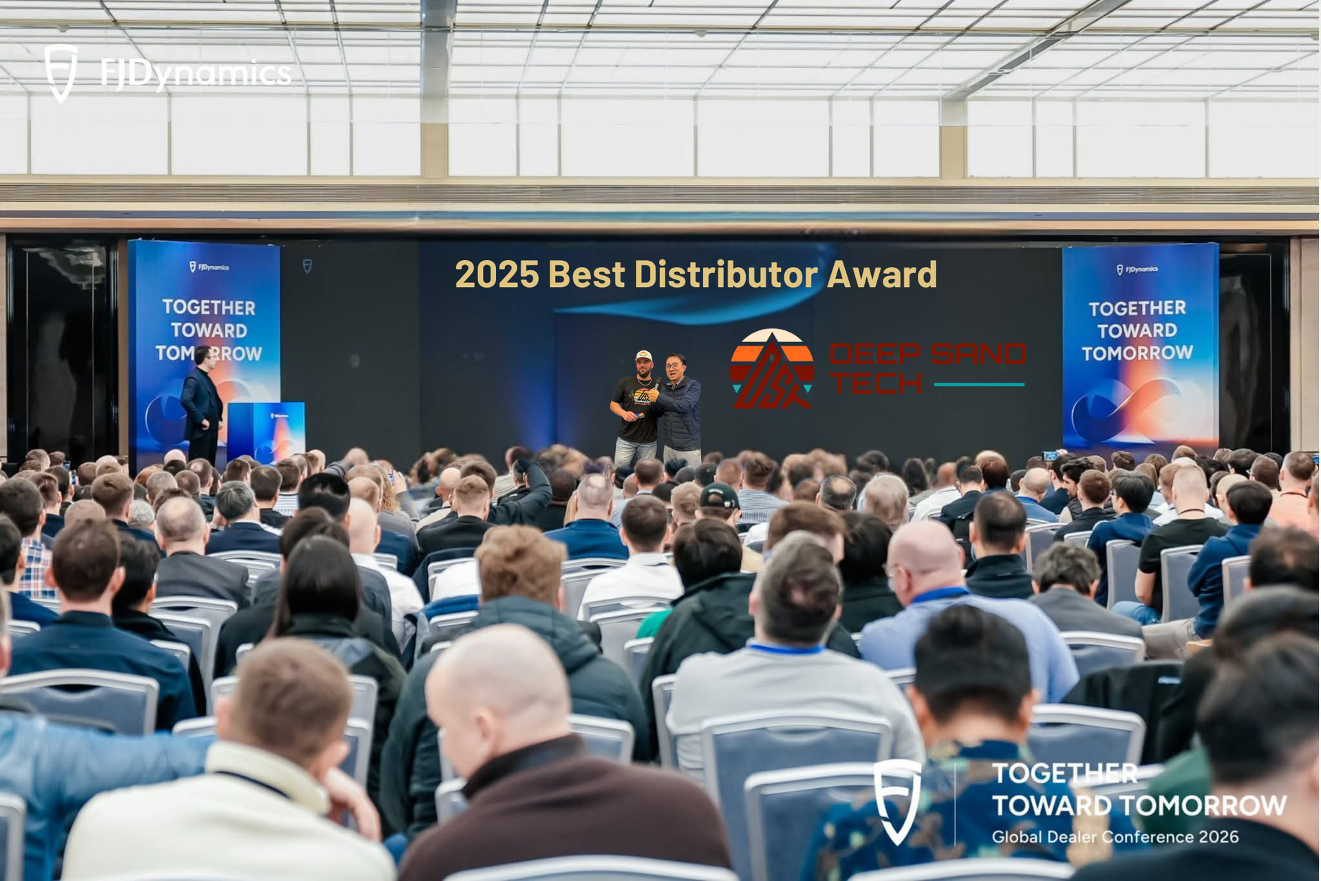 Two people stand on a stage presenting a 2025 Best Distributor Award to a large audience at a corporate conference.