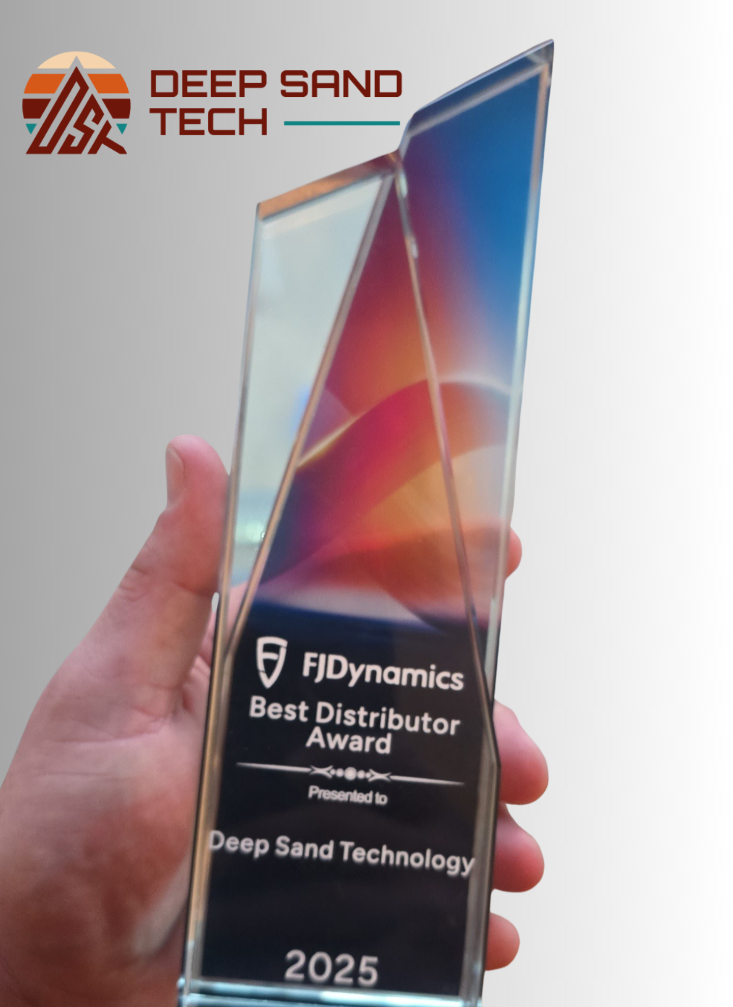 A hand holds a 2025 FJDynamics Best Distributor Award trophy presented to Deep Sand Technology.