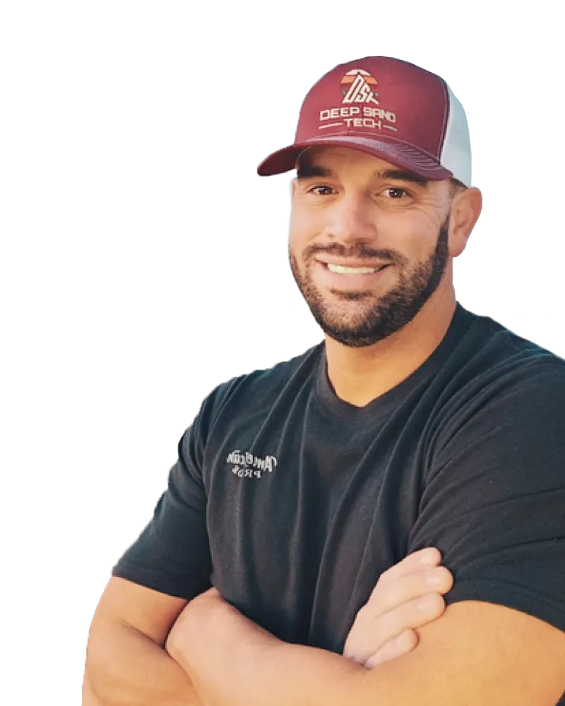 Man smiling, wearing a maroon and white cap, arms crossed. Dark shirt with logo.